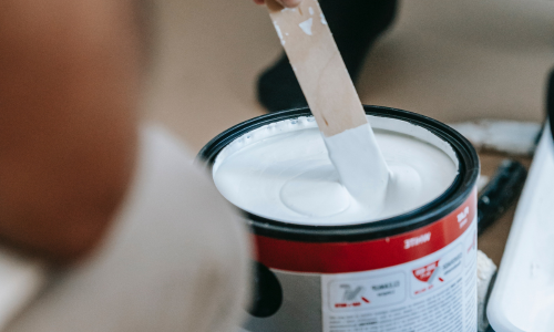 An open white paint can being stirred by a stir stick.
